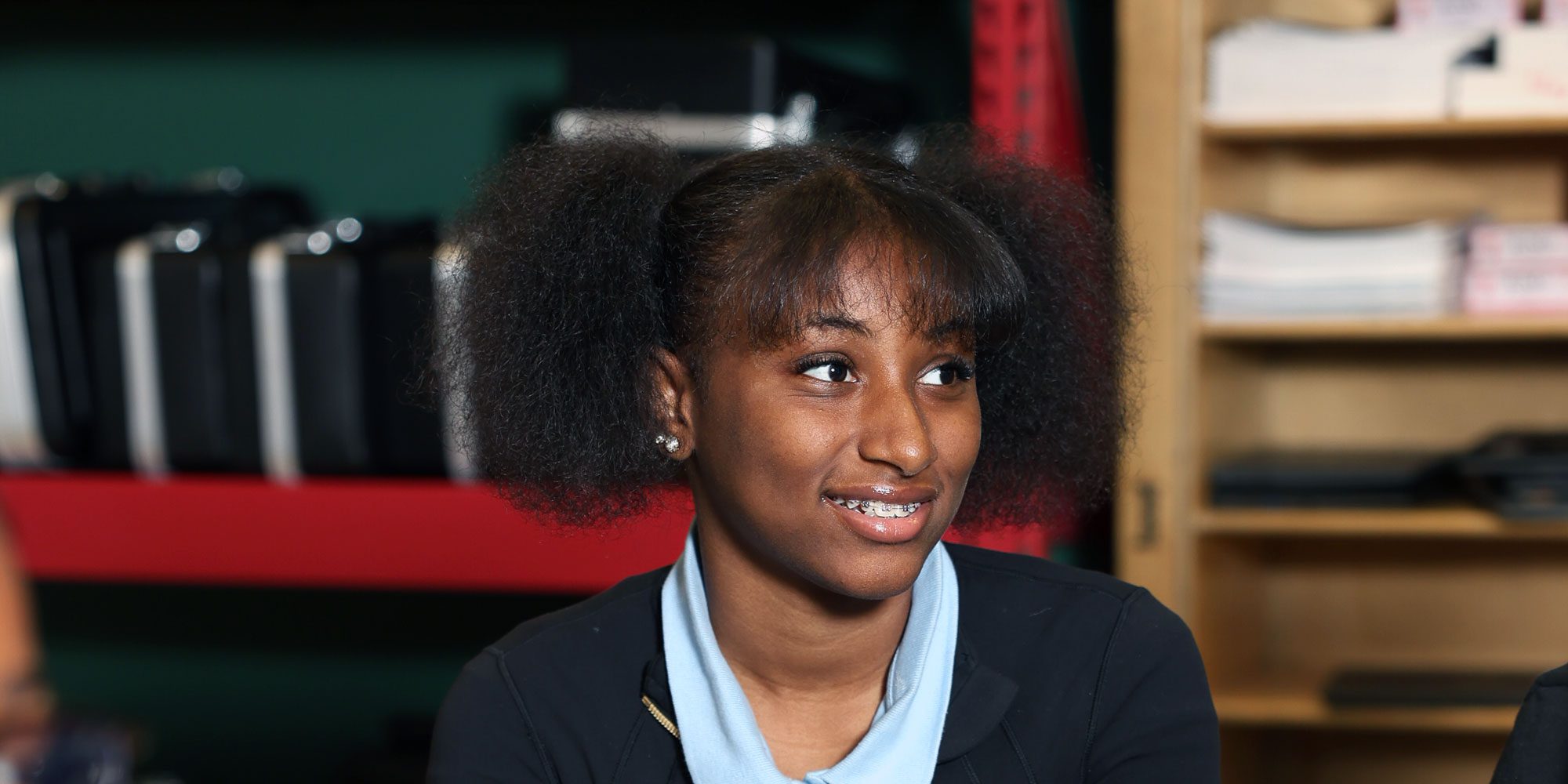 Smiling student in a school uniform in a classroom.