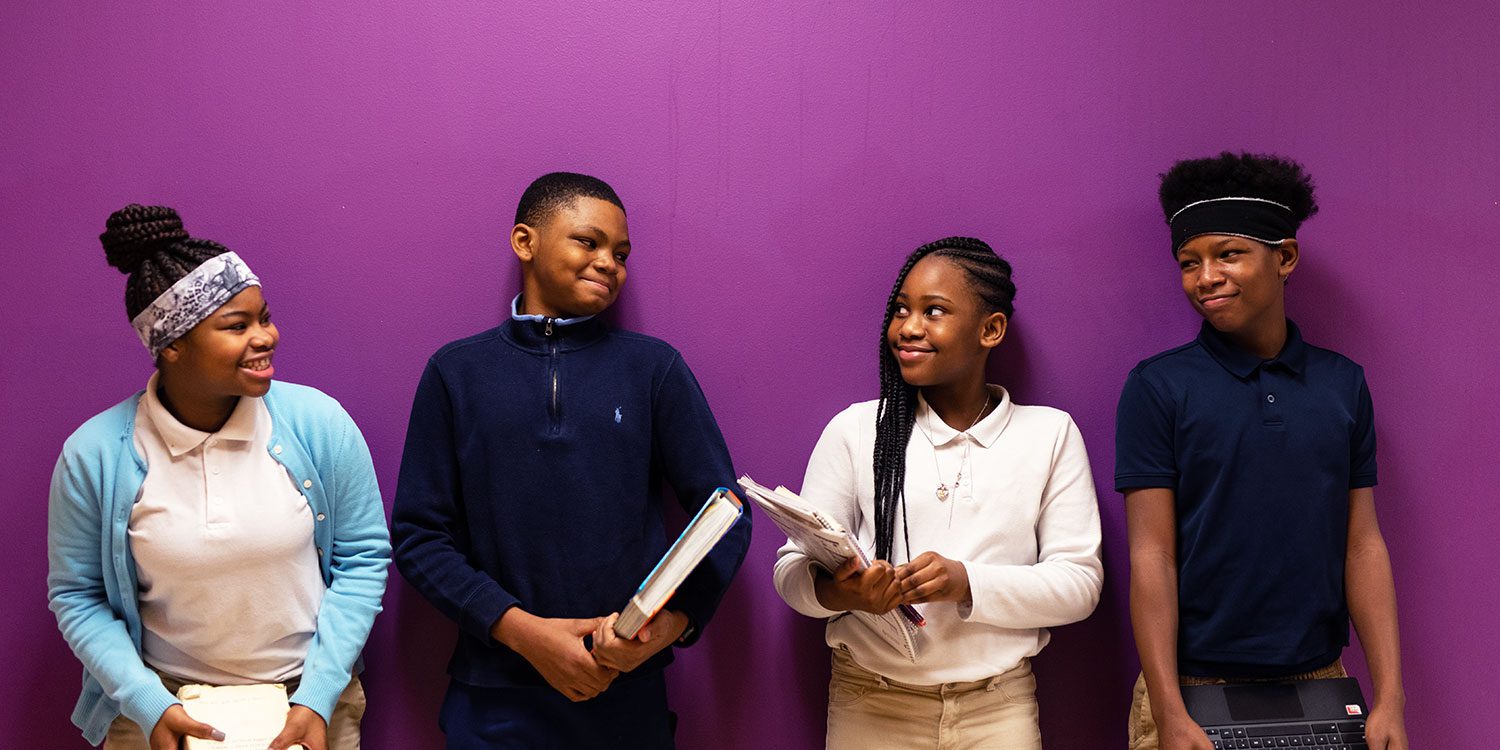 Smiling students standing next to each other against a purple wall.